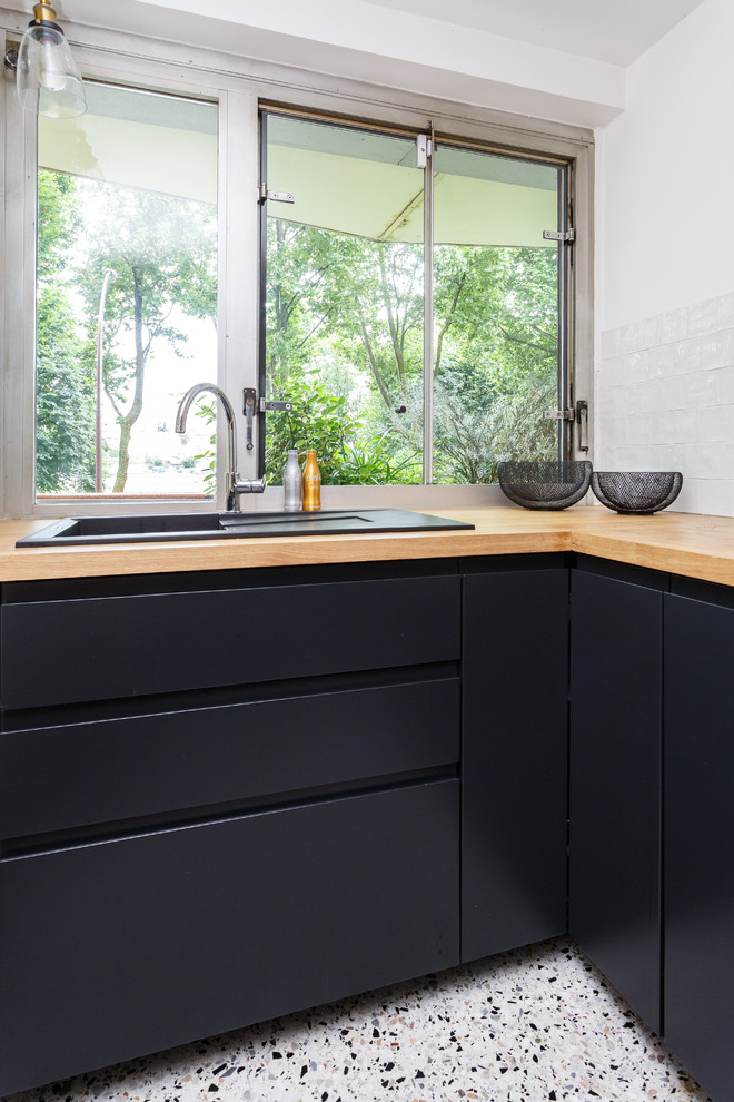 Photo of a small scandinavian l-shaped separate kitchen in Paris with a drop-in sink, flat-panel cabinets, black cabinets, wood benchtops, white splashback, ceramic splashback, stainless steel appliances, terrazzo floors, no island, multi-coloured floor and brown benchtop.