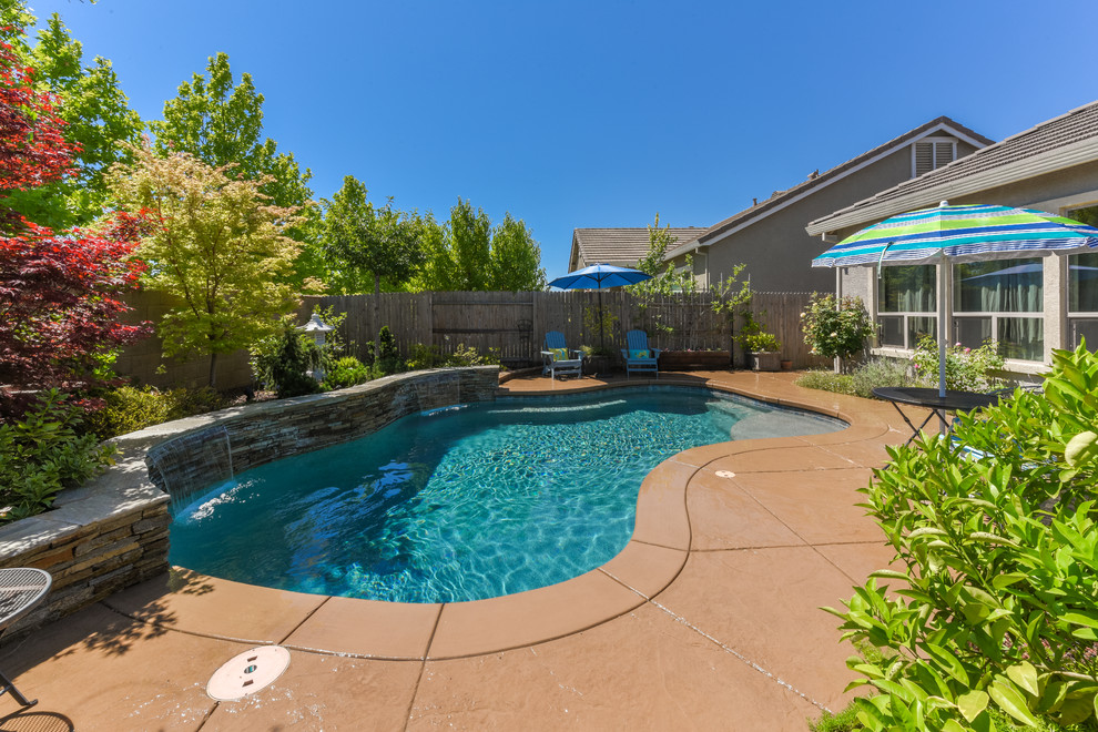 This is an example of a mid-sized tropical backyard custom-shaped pool in Sacramento with a water feature and natural stone pavers.