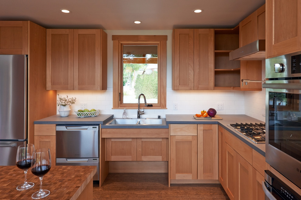 Inspiration for a mid-sized transitional l-shaped eat-in kitchen in Seattle with a double-bowl sink, shaker cabinets, medium wood cabinets, solid surface benchtops, white splashback, porcelain splashback, stainless steel appliances, medium hardwood floors and with island.