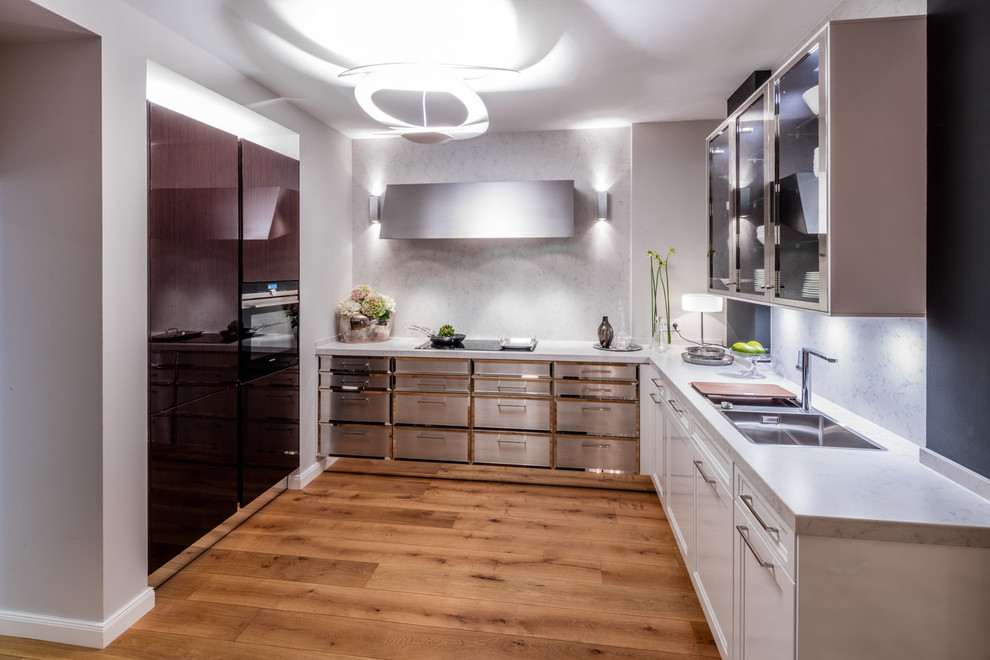 Photo of a mid-sized traditional u-shaped eat-in kitchen in Frankfurt with a single-bowl sink, beaded inset cabinets, solid surface benchtops, white splashback, stainless steel appliances and medium hardwood floors.