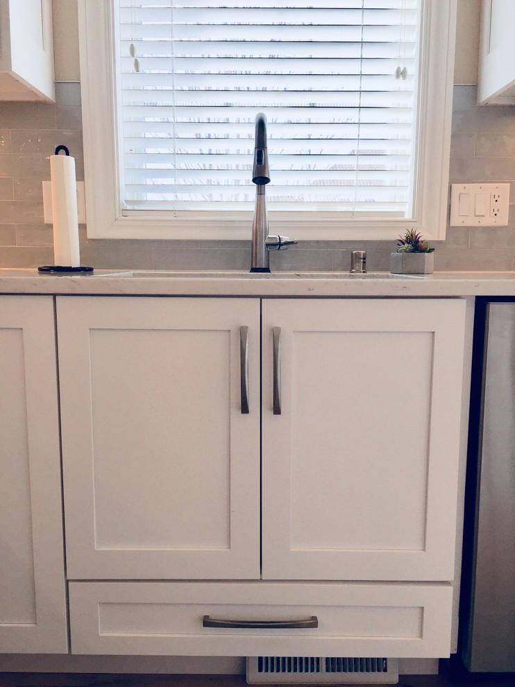 Mid-sized transitional light wood floor kitchen photo with an undermount sink, shaker cabinets, white cabinets, quartz countertops, blue backsplash, glass tile backsplash, stainless steel appliances and an island