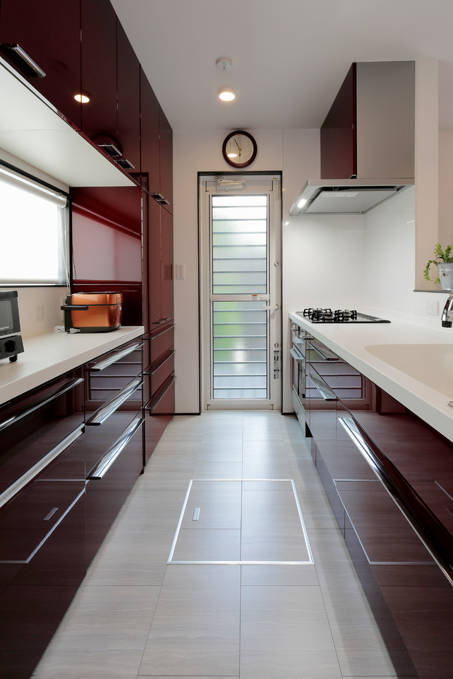 Design ideas for a contemporary single-wall kitchen in Tokyo with an integrated sink, flat-panel cabinets, red cabinets, white splashback, vinyl floors, a peninsula, grey floor and white benchtop.