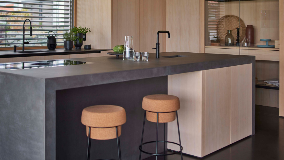 Cette image montre une cuisine ouverte design en bois clair avec un placard à porte plane, un plan de travail en béton, îlot, un sol noir et plan de travail noir.