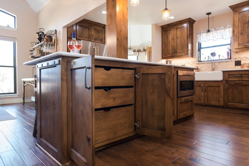 Example of a large transitional l-shaped brown floor and medium tone wood floor eat-in kitchen design in Dallas with a farmhouse sink, recessed-panel cabinets, medium tone wood cabinets, multicolored backsplash, an island, quartzite countertops, travertine backsplash, stainless steel appliances and white countertops