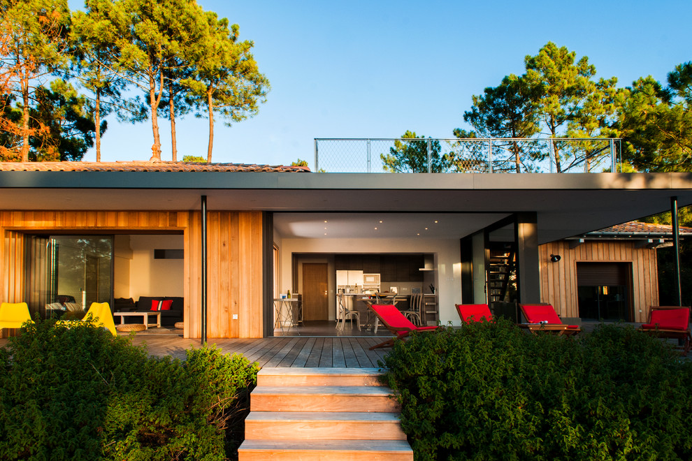 Photo of a large beach style one-storey brown exterior in Bordeaux with wood siding and a flat roof.