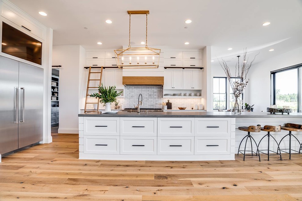 Inspiration for a country kitchen in Portland with shaker cabinets, white cabinets, grey splashback, subway tile splashback, stainless steel appliances, light hardwood floors, with island and grey benchtop.