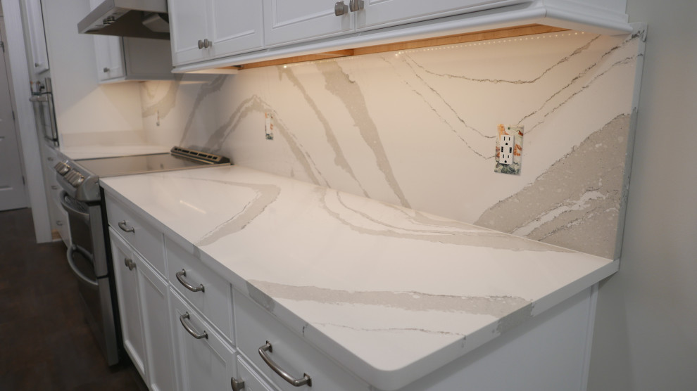 Example of a mid-sized transitional galley laminate floor and multicolored floor eat-in kitchen design with a farmhouse sink, shaker cabinets, white cabinets, quartz countertops, white backsplash, quartz backsplash, stainless steel appliances and white countertops