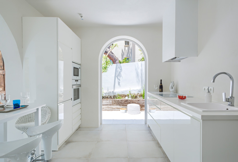 Photo of a mediterranean single-wall kitchen in Other with flat-panel cabinets, white cabinets, with island and white benchtop.