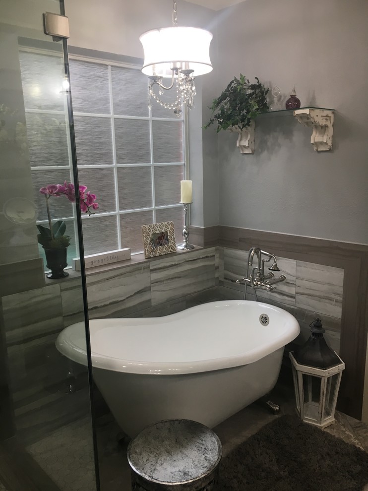 Photo of a transitional master bathroom in Houston with furniture-like cabinets, grey cabinets, a claw-foot tub, a corner shower, a two-piece toilet, gray tile, porcelain tile, grey walls, porcelain floors, an undermount sink, marble benchtops, grey floor, a hinged shower door and grey benchtops.