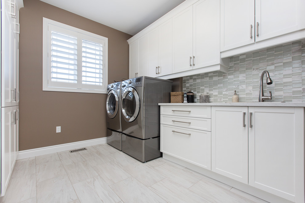 This is an example of a mid-sized transitional galley dedicated laundry room in Toronto with an undermount sink, shaker cabinets, white cabinets, laminate benchtops, beige walls, ceramic floors and a side-by-side washer and dryer.