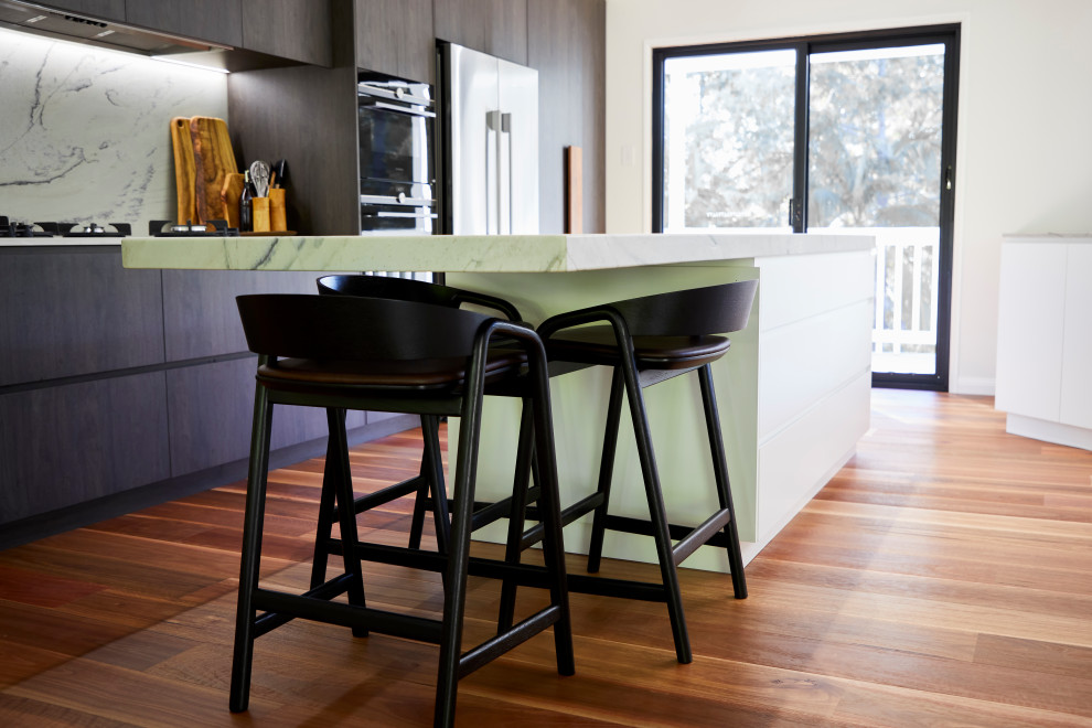 Inspiration for a large modern galley eat-in kitchen in Sunshine Coast with an integrated sink, raised-panel cabinets, dark wood cabinets, marble benchtops, white splashback, marble splashback, stainless steel appliances, light hardwood floors, with island, brown floor and white benchtop.