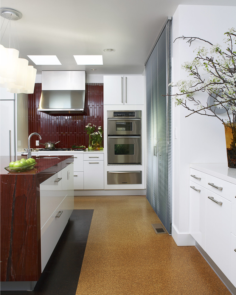 Inspiration for a mid-sized modern u-shaped eat-in kitchen in San Francisco with stainless steel appliances, orange floor, a drop-in sink, flat-panel cabinets, white cabinets, granite benchtops, red splashback, ceramic splashback, cork floors, with island and red benchtop.