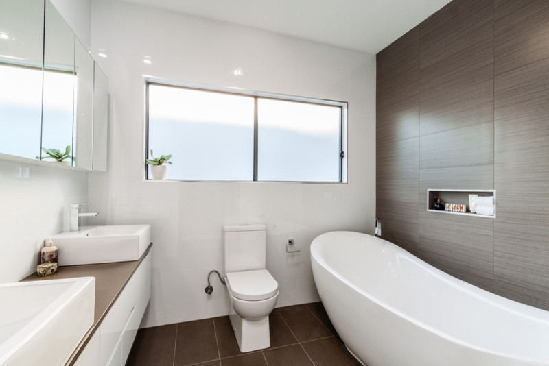 This is an example of a small modern master bathroom in Sydney with a vessel sink, white cabinets, engineered quartz benchtops, a freestanding tub, a one-piece toilet, ceramic tile, white walls, ceramic floors and gray tile.