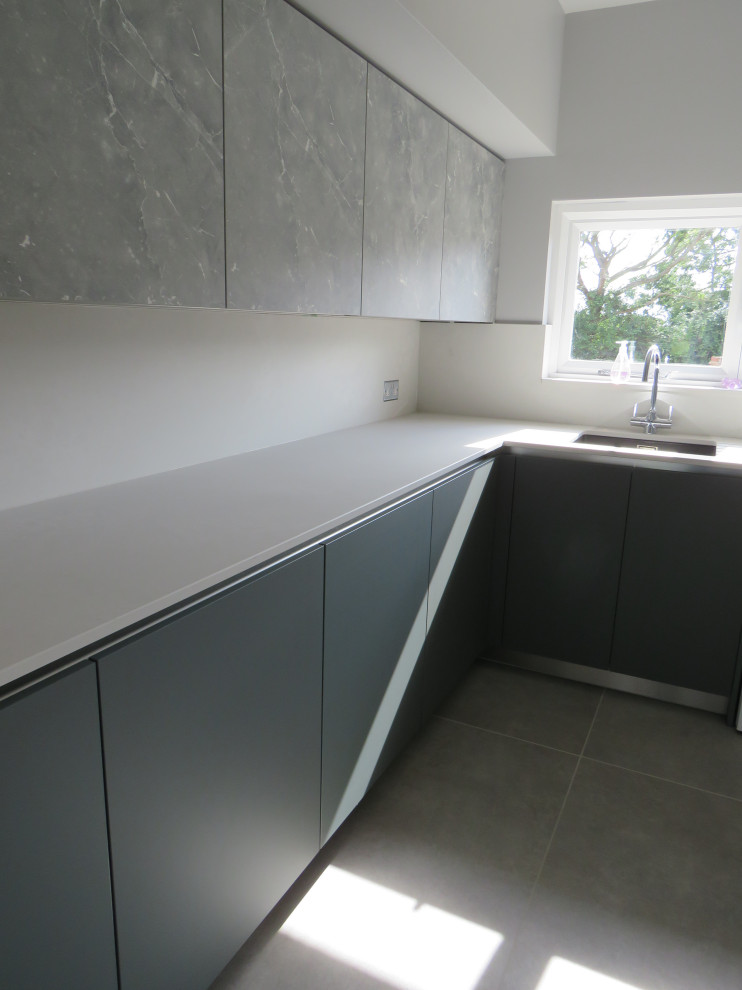 Mid-sized modern l-shaped laundry room in Essex with an undermount sink, flat-panel cabinets, green cabinets, quartzite benchtops, white splashback, engineered quartz splashback, grey walls, porcelain floors, a side-by-side washer and dryer, grey floor and white benchtop.