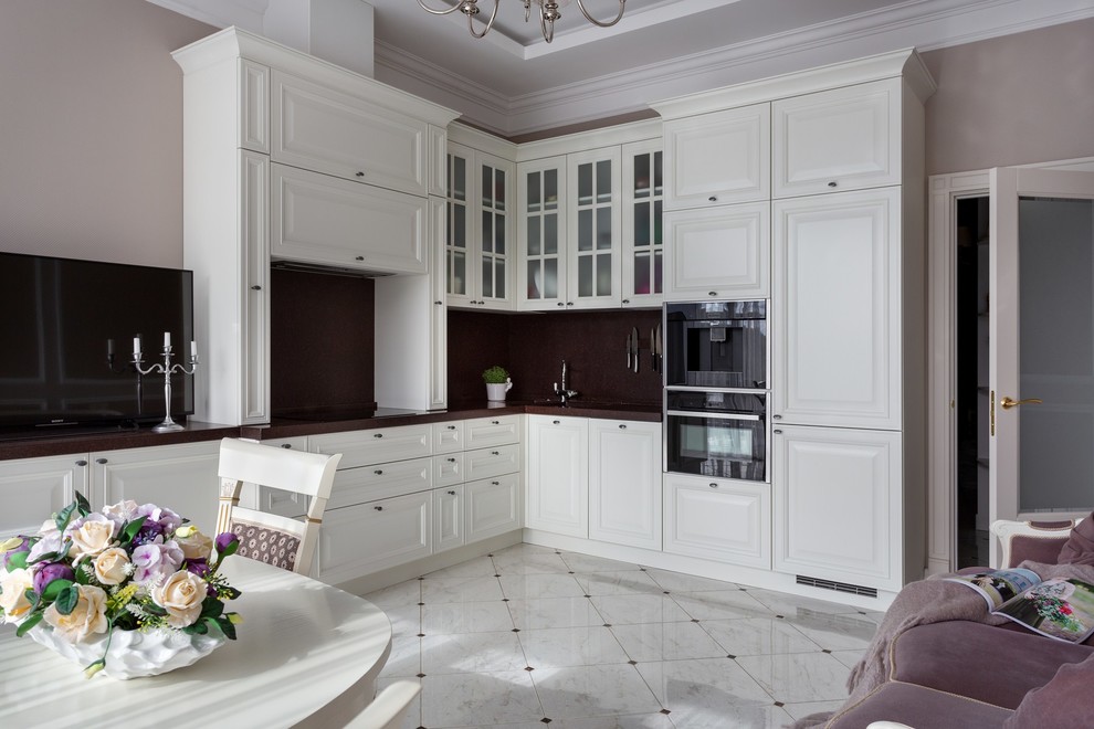Transitional l-shaped open plan kitchen in Moscow with raised-panel cabinets, white cabinets, brown splashback, black appliances, no island, white floor and brown benchtop.
