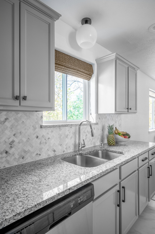 Bild på ett mellanstort vintage grå grått kök, med en undermonterad diskho, luckor med infälld panel, grå skåp, granitbänkskiva, vitt stänkskydd, stänkskydd i marmor, rostfria vitvaror, klinkergolv i porslin, en halv köksö och vitt golv