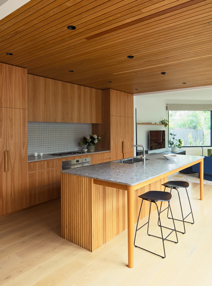 Large trendy medium tone wood floor and wood ceiling eat-in kitchen photo in Melbourne with flat-panel cabinets, light wood cabinets, granite countertops, beige backsplash, mosaic tile backsplash, stainless steel appliances, an island and multicolored countertops