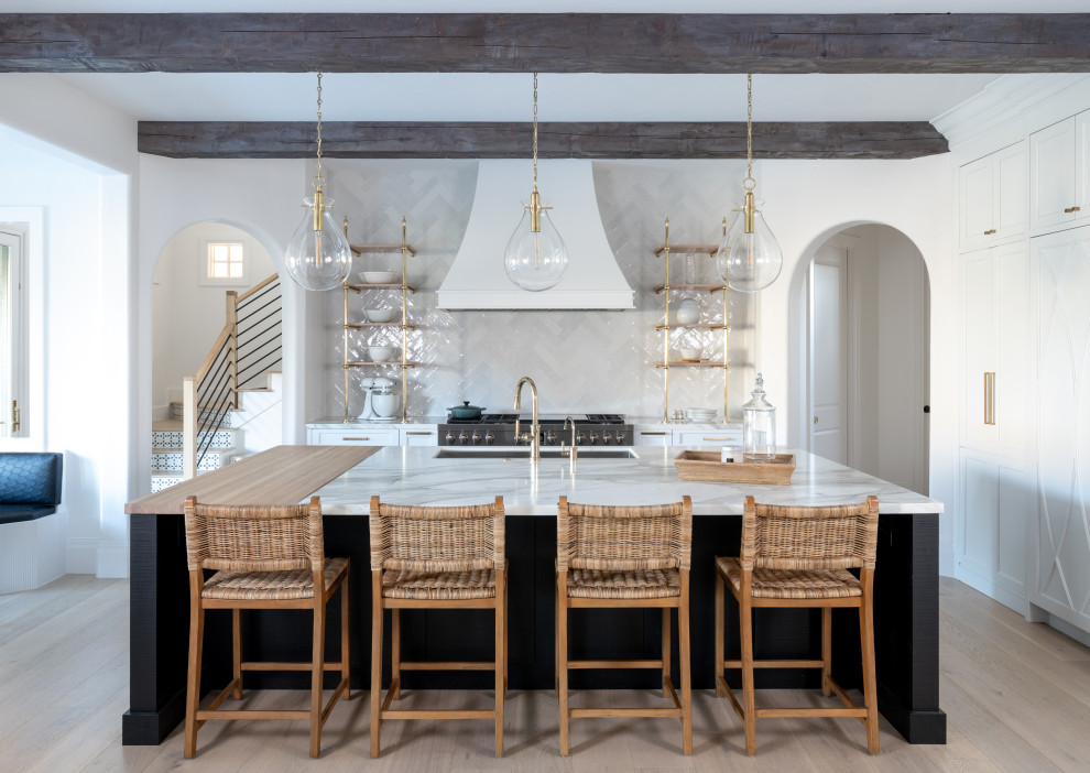 Transitional l-shaped light wood floor, beige floor and exposed beam kitchen photo in Dallas with an undermount sink, recessed-panel cabinets, white cabinets, white backsplash, stainless steel appliances, an island and white countertops
