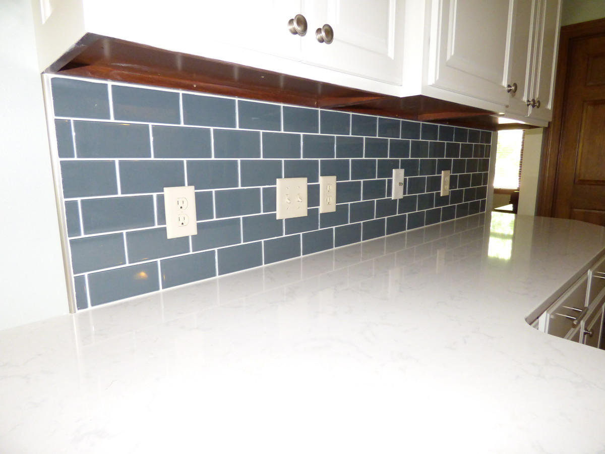 Mid-sized transitional l-shaped ceramic tile and gray floor eat-in kitchen photo with an undermount sink, raised-panel cabinets, white cabinets, quartz countertops, blue backsplash, subway tile backsplash, stainless steel appliances and a peninsula