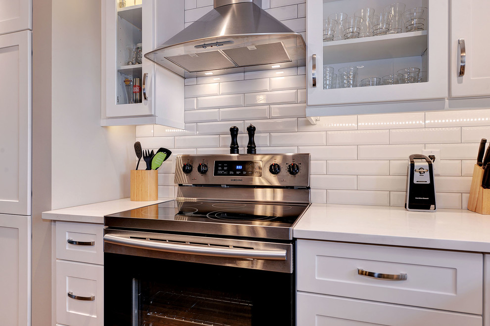 Example of a transitional dark wood floor and brown floor enclosed kitchen design with a single-bowl sink, shaker cabinets, white cabinets, quartzite countertops, white backsplash, subway tile backsplash, stainless steel appliances and an island