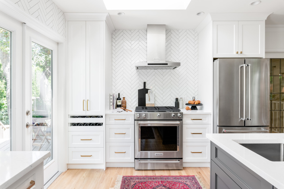 Large transitional l-shaped light wood floor and beige floor open concept kitchen photo in Vancouver with an undermount sink, recessed-panel cabinets, white cabinets, quartz countertops, white backsplash, ceramic backsplash, stainless steel appliances, an island and white countertops