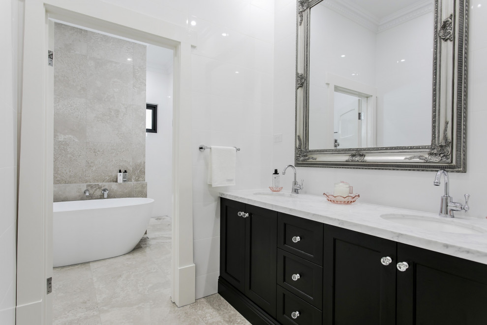 Klassisk inredning av ett stort vit vitt en-suite badrum, med möbel-liknande, svarta skåp, ett fristående badkar, en öppen dusch, vit kakel, klinkergolv i keramik, ett nedsänkt handfat, marmorbänkskiva, grått golv och med dusch som är öppen
