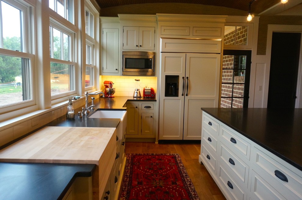 This is an example of a large traditional u-shaped kitchen in Milwaukee with a farmhouse sink, flat-panel cabinets, green cabinets, granite benchtops, white splashback, ceramic splashback, stainless steel appliances, medium hardwood floors and with island.