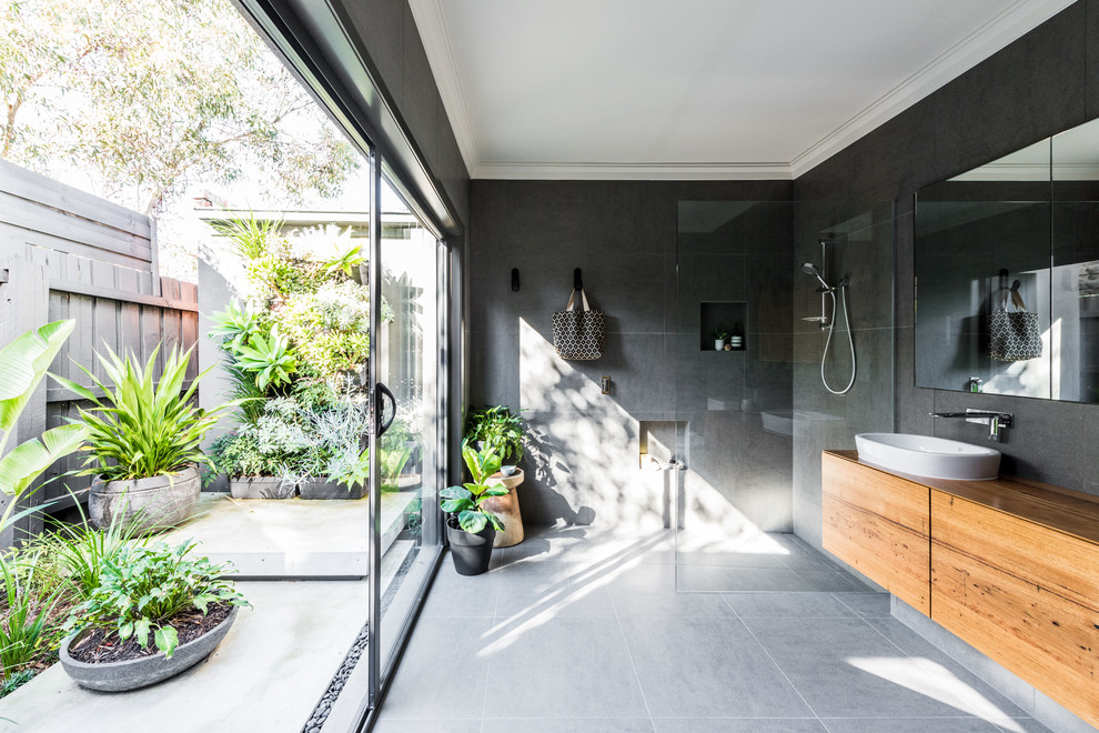 Contemporary bathroom in Melbourne with medium wood cabinets, an alcove shower, gray tile, grey walls, a vessel sink, wood benchtops, grey floor, an open shower and brown benchtops.