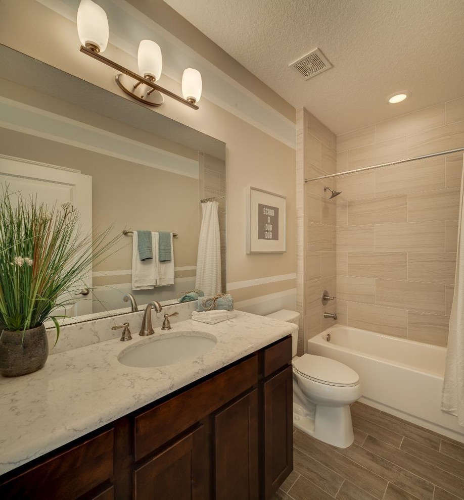 Photo of a mid-sized traditional 3/4 bathroom in Jacksonville with shaker cabinets, dark wood cabinets, an alcove tub, a shower/bathtub combo, a two-piece toilet, beige walls, laminate floors, an undermount sink, marble benchtops and a shower curtain.