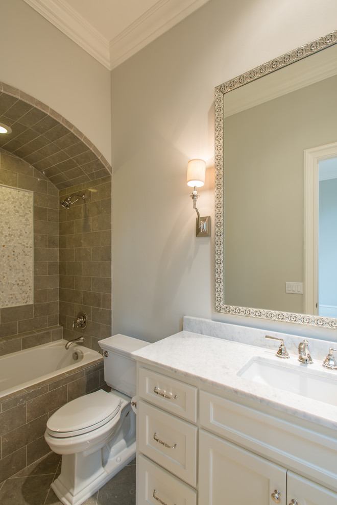 Photo of a mid-sized mediterranean kids bathroom in Dallas with raised-panel cabinets, white cabinets, a drop-in tub, an alcove shower, a two-piece toilet, grey walls, limestone floors, an undermount sink, marble benchtops, grey floor and an open shower.
