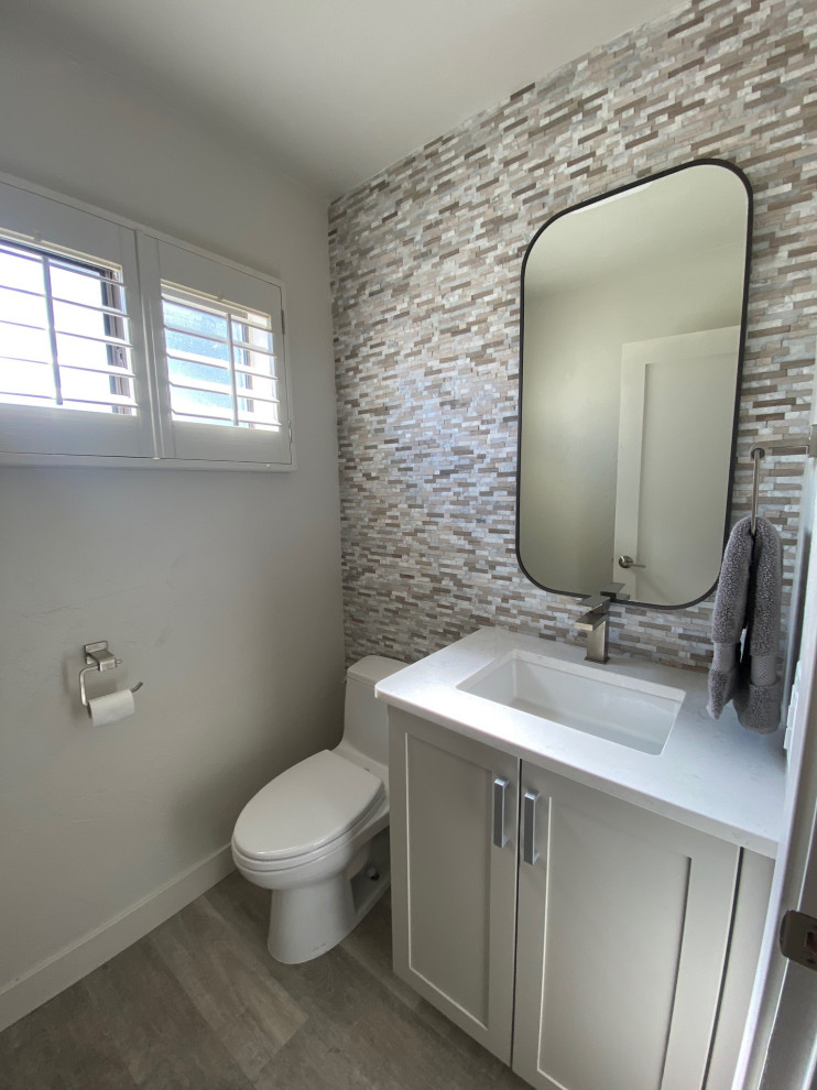 Inredning av ett klassiskt litet vit vitt toalett, med släta luckor, vita skåp, en toalettstol med hel cisternkåpa, grå kakel, mosaik, grå väggar, vinylgolv, ett undermonterad handfat, bänkskiva i kvarts och grått golv