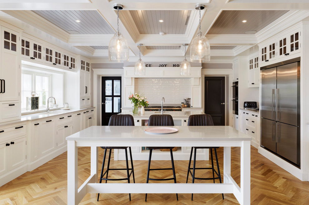Inspiration for a large beach style kitchen in Hertfordshire with shaker cabinets, white cabinets, quartzite benchtops, white splashback, subway tile splashback, stainless steel appliances, light hardwood floors, multiple islands, grey benchtop, an undermount sink and beige floor.