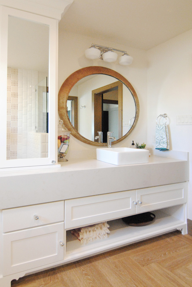 This is an example of a mid-sized eclectic kids bathroom with recessed-panel cabinets, white cabinets, a drop-in tub, a shower/bathtub combo, a two-piece toilet, white tile, subway tile, white walls, vinyl floors, a vessel sink, engineered quartz benchtops, brown floor and an open shower.