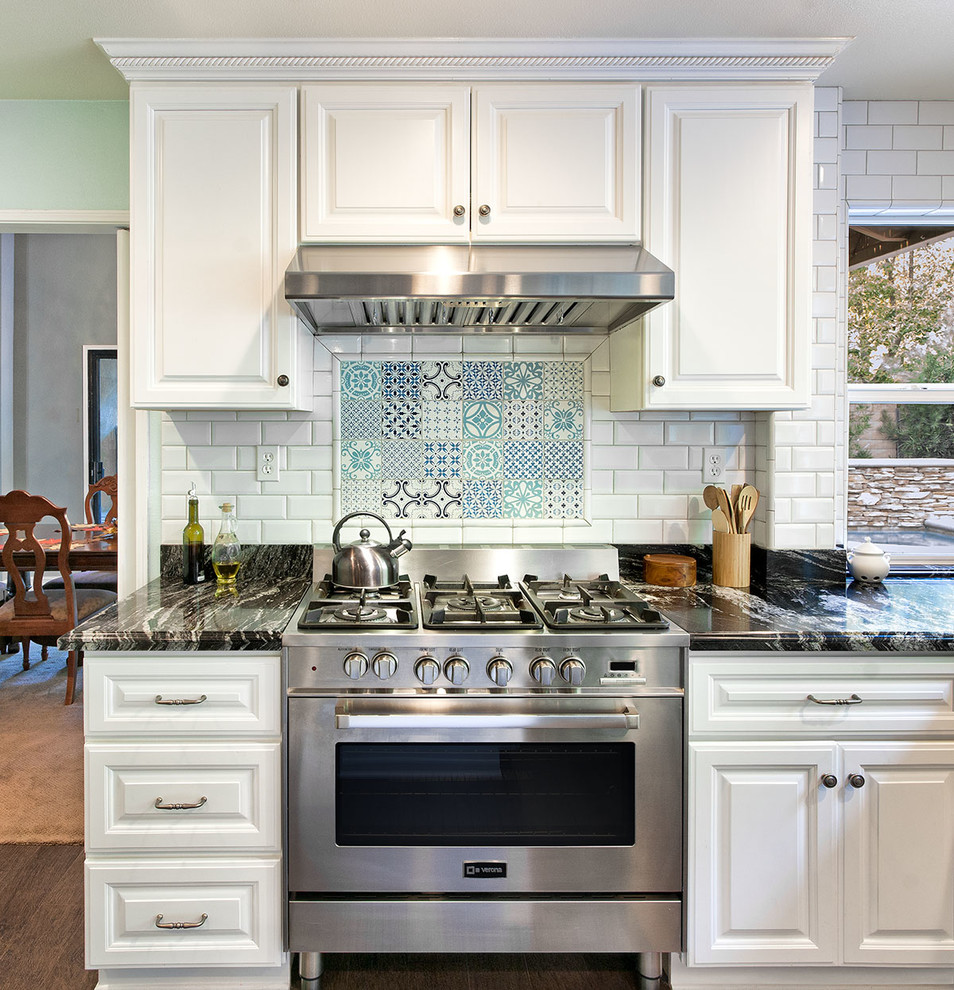 This is an example of a traditional kitchen in Orange County with raised-panel cabinets, white cabinets, white splashback, subway tile splashback, stainless steel appliances and dark hardwood floors.