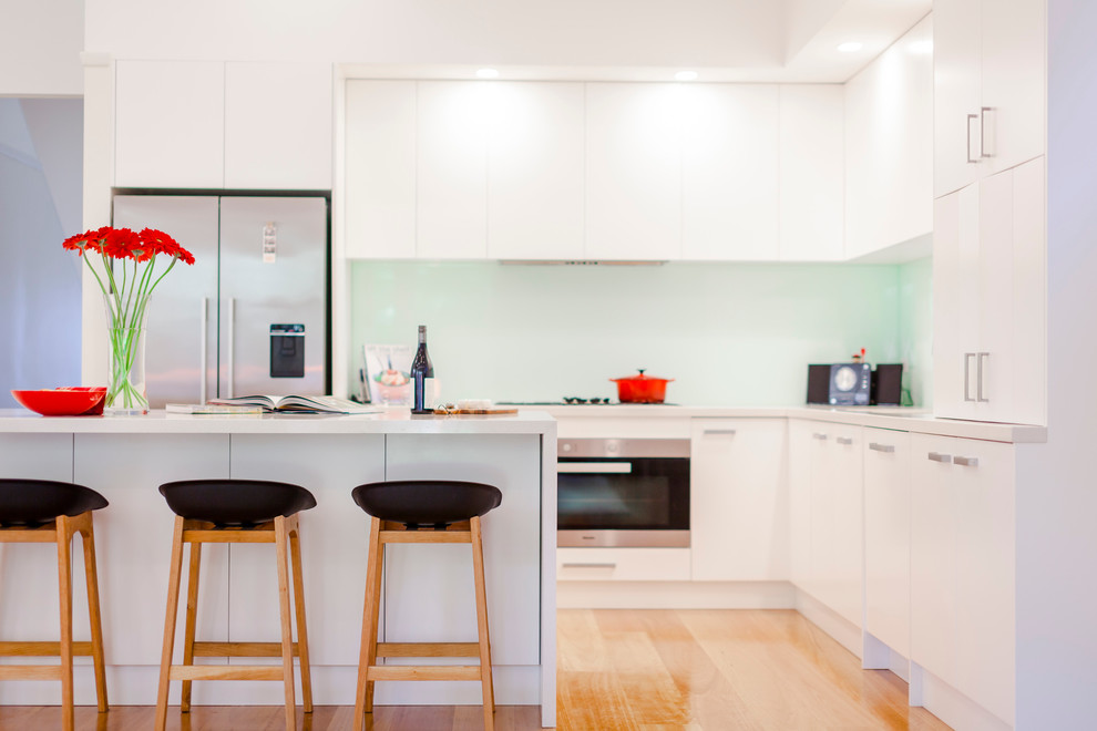 Inspiration for a large contemporary l-shaped eat-in kitchen in Melbourne with an undermount sink, flat-panel cabinets, white cabinets, quartz benchtops, blue splashback, glass sheet splashback, stainless steel appliances, medium hardwood floors and with island.