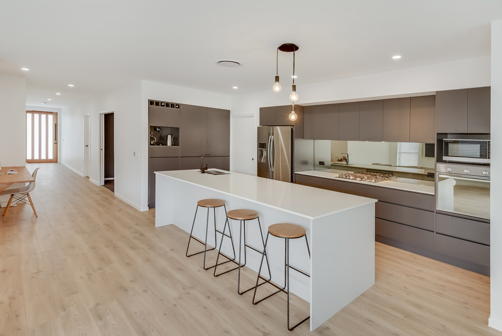 Photo of a contemporary l-shaped eat-in kitchen in Sunshine Coast with a drop-in sink, black cabinets, quartzite benchtops, black splashback, mirror splashback, stainless steel appliances and vinyl floors.