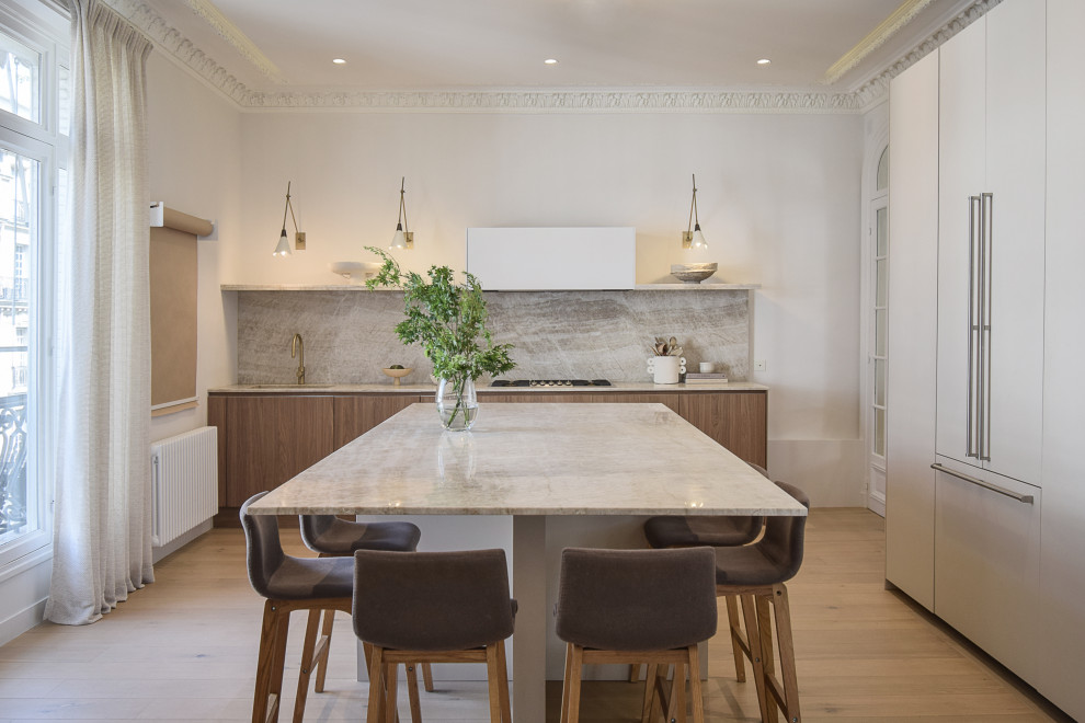 Large contemporary open plan kitchen in Paris with an integrated sink, flat-panel cabinets, dark wood cabinets, marble benchtops, white splashback, marble splashback, panelled appliances, light hardwood floors, with island and white benchtop.