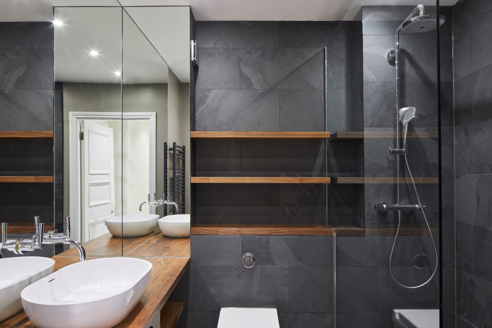 Mid-sized contemporary 3/4 bathroom in London with open cabinets, medium wood cabinets, an open shower, a wall-mount toilet, gray tile, slate, grey walls, limestone floors, a console sink, wood benchtops, beige floor, an open shower, brown benchtops, a niche, a single vanity and a built-in vanity.