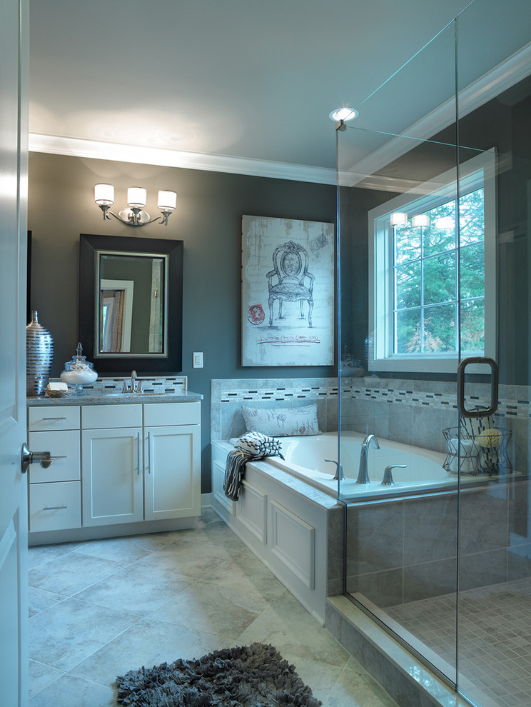 Example of a mid-sized transitional master gray tile and ceramic tile ceramic tile drop-in bathtub design with shaker cabinets, white cabinets, granite countertops, gray walls, an undermount sink and a one-piece toilet