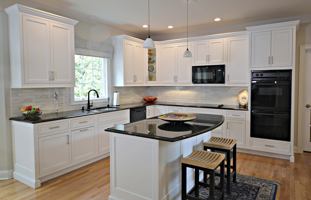 This is an example of a large transitional l-shaped eat-in kitchen in New York with an undermount sink, beaded inset cabinets, white cabinets, granite benchtops, beige splashback, porcelain splashback, black appliances, medium hardwood floors, with island, brown floor and black benchtop.