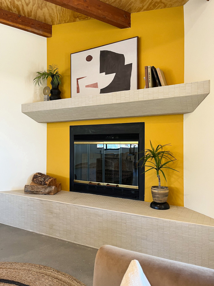 Amerikansk inredning av ett vardagsrum, med gula väggar, betonggolv, en öppen hörnspis, en spiselkrans i trä och grått golv