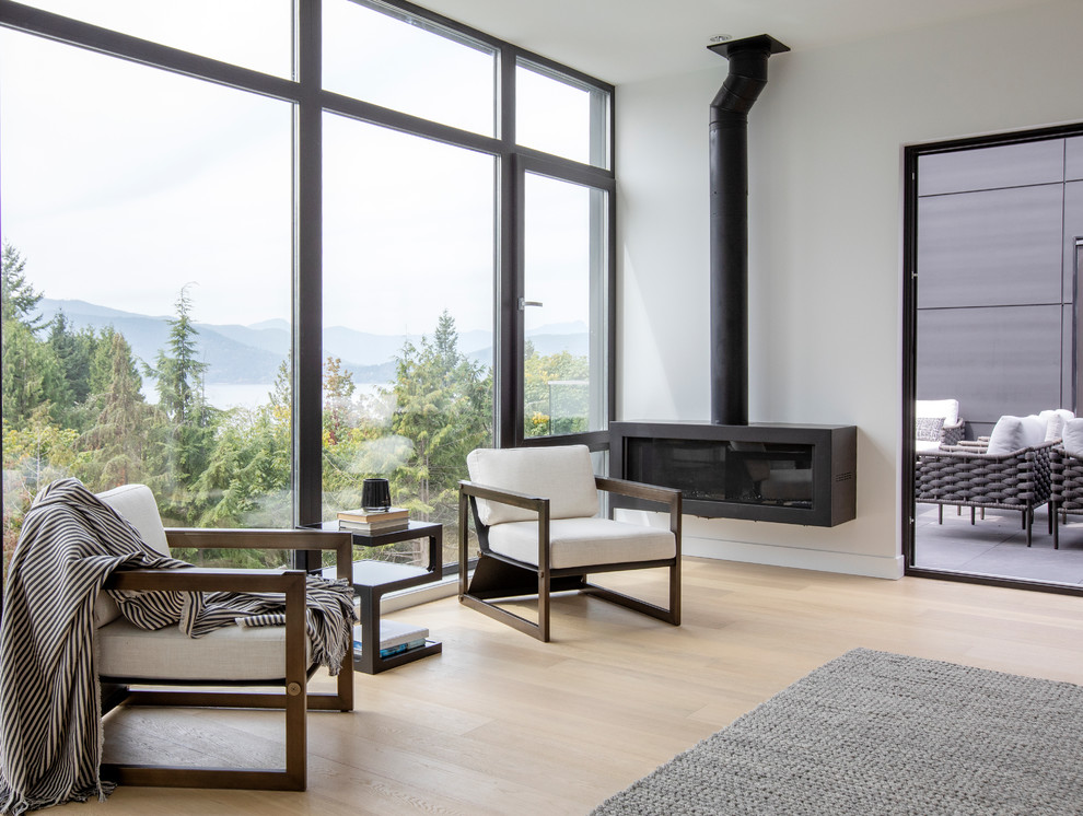 Large modern master bedroom in Vancouver with white walls, light hardwood floors, a hanging fireplace, a metal fireplace surround and beige floor.