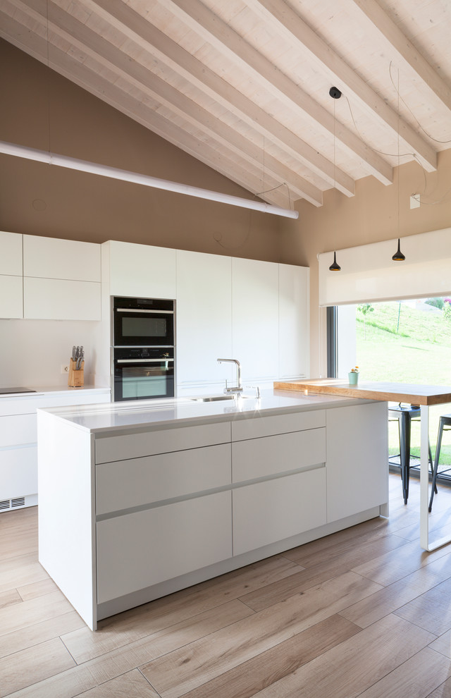 This is an example of a contemporary open plan kitchen in Other with an undermount sink, flat-panel cabinets, white cabinets, quartz benchtops, white splashback, black appliances, with island and brown floor.