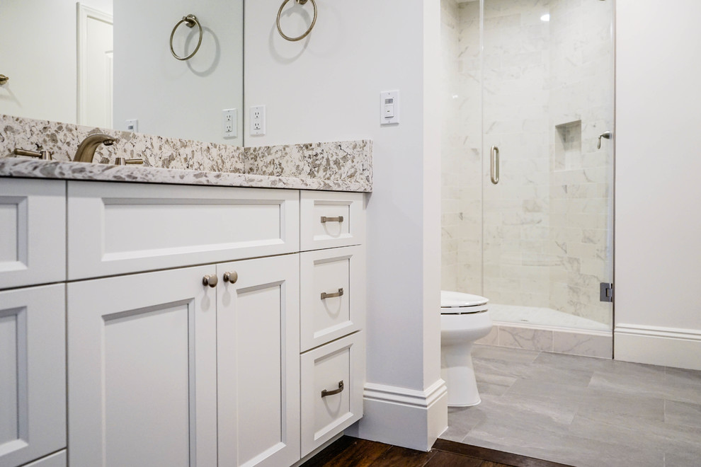 Photo of a mid-sized contemporary master bathroom in Los Angeles with white cabinets, an alcove shower, a two-piece toilet, beige tile, white walls, dark hardwood floors, a drop-in sink, brown floor, a hinged shower door, multi-coloured benchtops, recessed-panel cabinets, ceramic tile, engineered quartz benchtops, a niche, a built-in vanity and a double vanity.