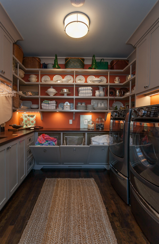 This is an example of a mid-sized galley utility room in Charleston with grey cabinets, wood benchtops, orange walls, dark hardwood floors, a side-by-side washer and dryer and brown benchtop.