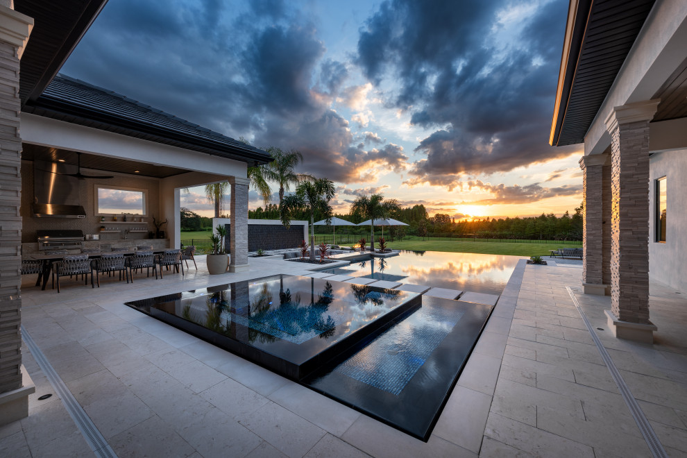 This is an example of an expansive modern backyard custom-shaped infinity pool in Tampa with tile and a hot tub.