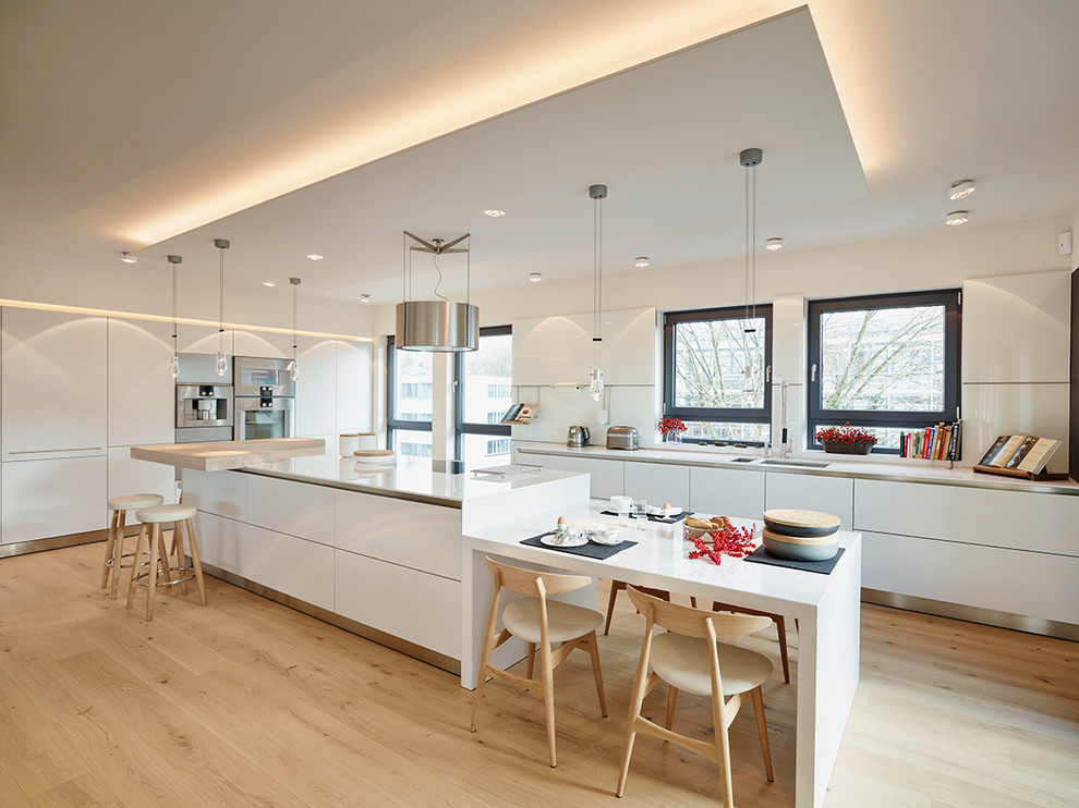 Large contemporary eat-in kitchen in Frankfurt with an undermount sink, flat-panel cabinets, white cabinets, stainless steel appliances, light hardwood floors, with island and white splashback.