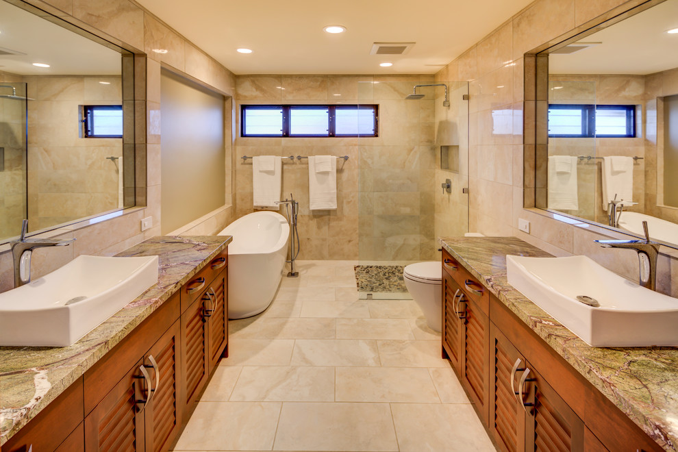 Photo of a large tropical bathroom in Hawaii with louvered cabinets, medium wood cabinets, a freestanding tub, a curbless shower, a two-piece toilet, beige tile, beige walls and a vessel sink.