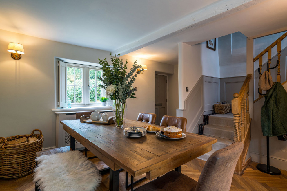 This is an example of a mid-sized country dining room in Gloucestershire with grey walls, dark hardwood floors, a two-sided fireplace, a plaster fireplace surround, brown floor and panelled walls.