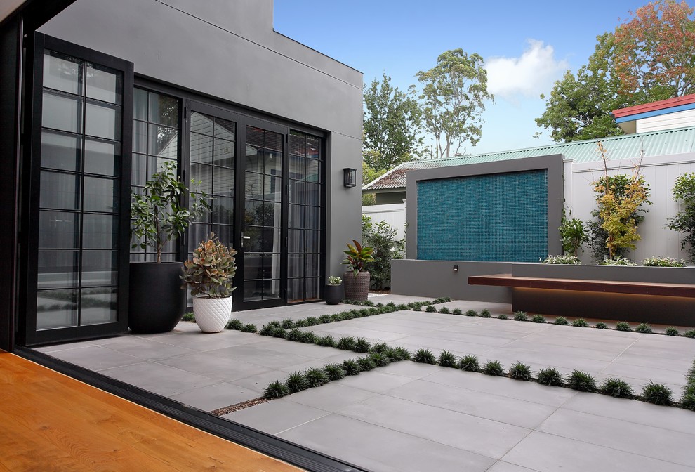 Large contemporary courtyard shaded formal garden in Sydney with a water feature and natural stone pavers for winter.